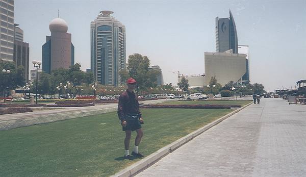 Tourist standing on the corniche lawn with skyscrapers and palm trees behind