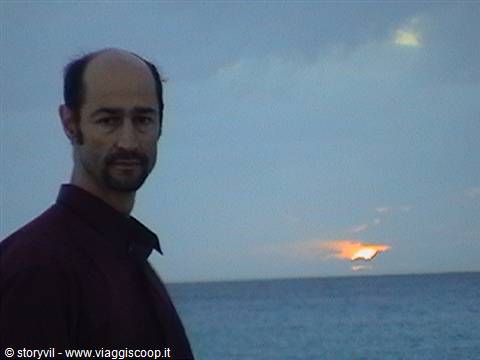 Man in dark shirt by the sea with low sun among clouds