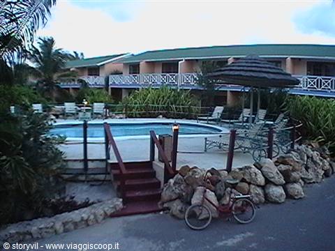 Resort pool with loungers, thatched umbrella and a bicycle leaning on rocks