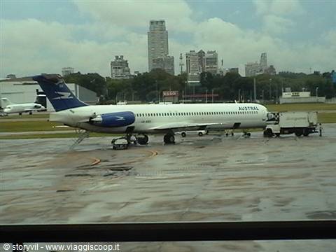 Austral MD-81 jet parked on wet tarmac with Buenos Aires skyscrapers behind