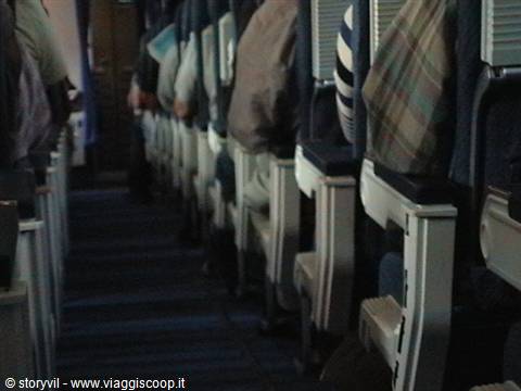 Airplane cabin interior, passengers seated in blue seats, dim aisle light
