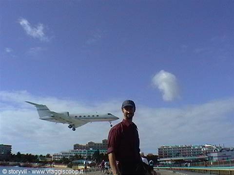 Man in cap next to a jet landing low over the beach
