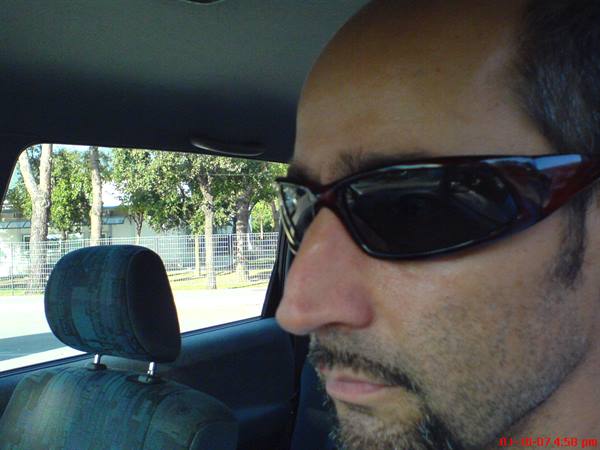 Man wearing sunglasses driving a car, trees visible through the window