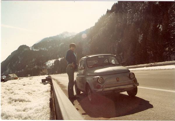 Man standing beside a parked Fiat 500 on a snowy mountain roadside