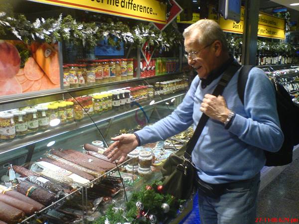 Man with backpack choosing sausages and jarred goods at a deli counter