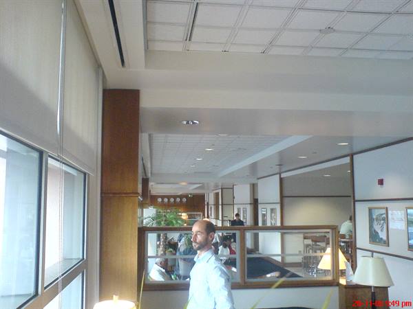 Man in light blue shirt walks through an indoor lobby with wood panels and lamps