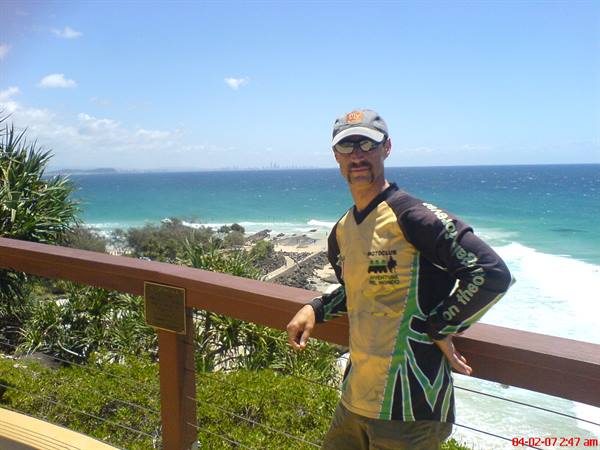 Man in cap and yellow jersey leans on wooden railing above a turquoise beach