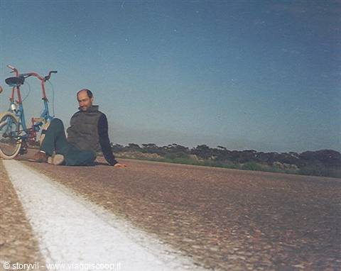 Man sitting on the asphalt next to a red bicycle on a country road