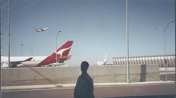 Qantas plane taking off near airport terminal, blurred man in foreground