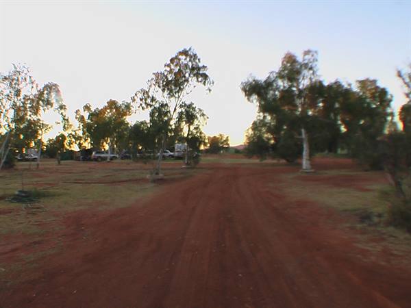 Red dirt road among trees and camper campsite, low light