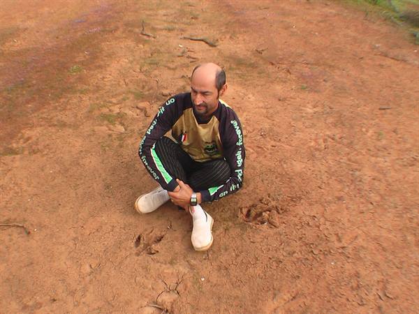 Man crouching on red muddy ground, looking at animal tracks