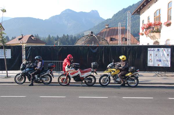 Three motorcyclists with helmets stopped on a road in front of mountains