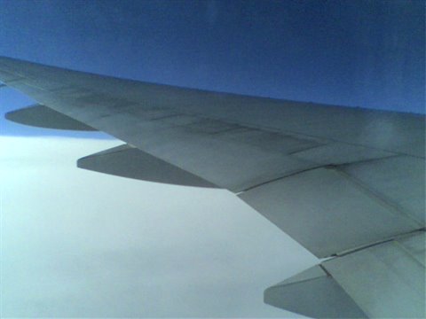 Gray airplane wing above white clouds, deep blue sky