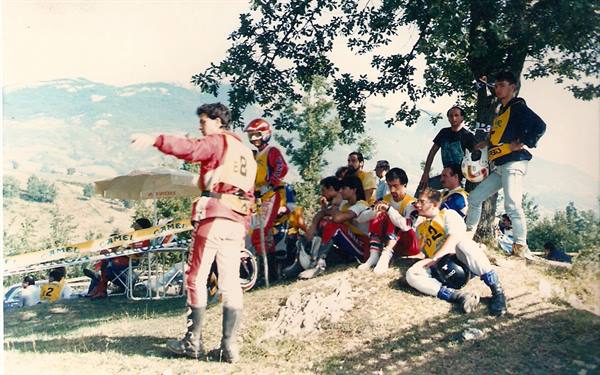 Motocross riders in yellow and red suits resting under trees