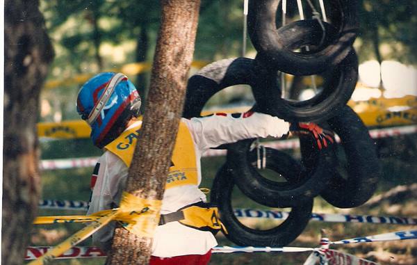Motocross rider in blue helmet and yellow vest grabbing suspended tires between trees