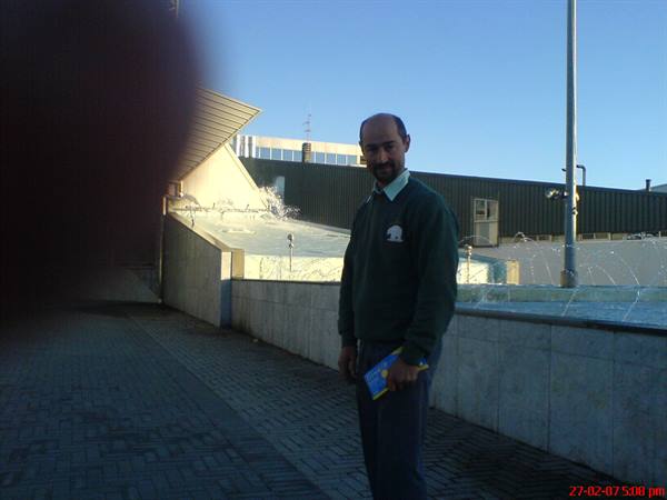 Smiling man in green sweater beside a concrete fountain, late afternoon light