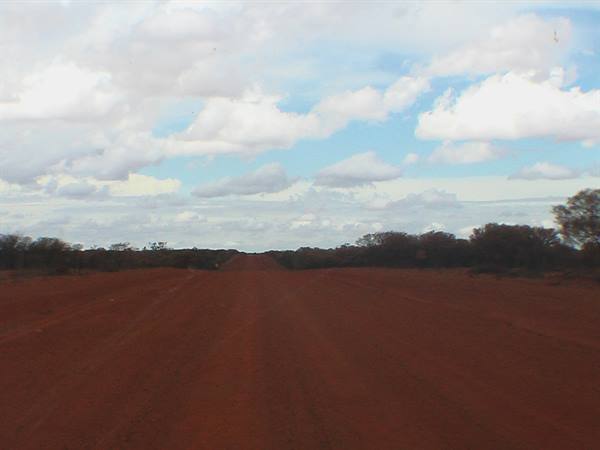 Red dirt road through scrub under cloudy sky, Australian outback