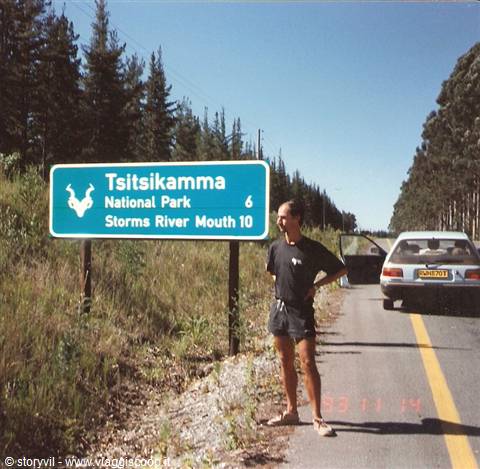 Tourist beside the green Tsitsikamma National Park sign, car parked on the road