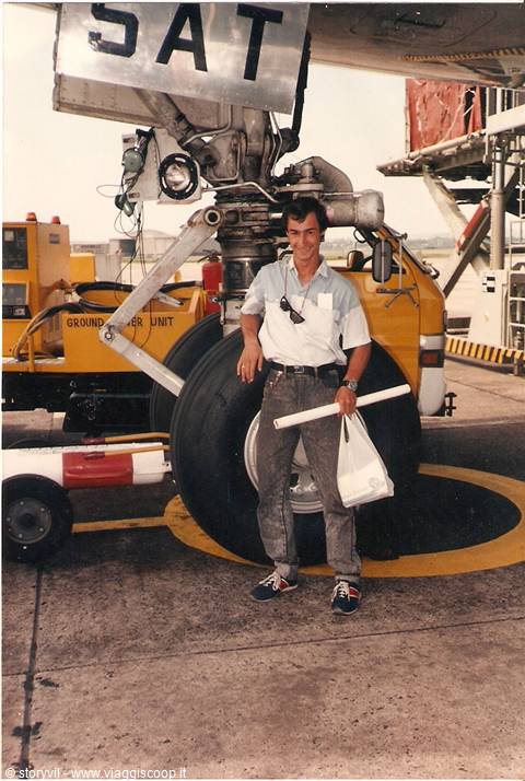 Young man beside an airplane landing gear, holding a bag, on the tarmac