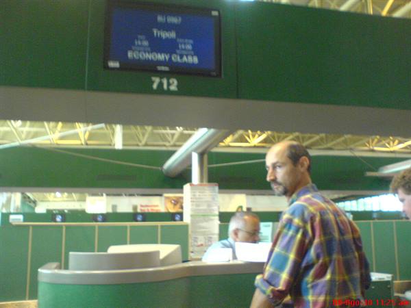 Man in plaid shirt at check-in counter 712, blue economy class screen