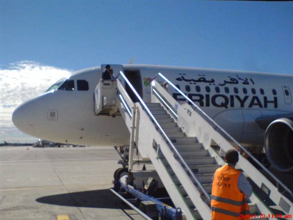 Afriqiyah aircraft on the apron, metal boarding stairs, ground crew in orange vest