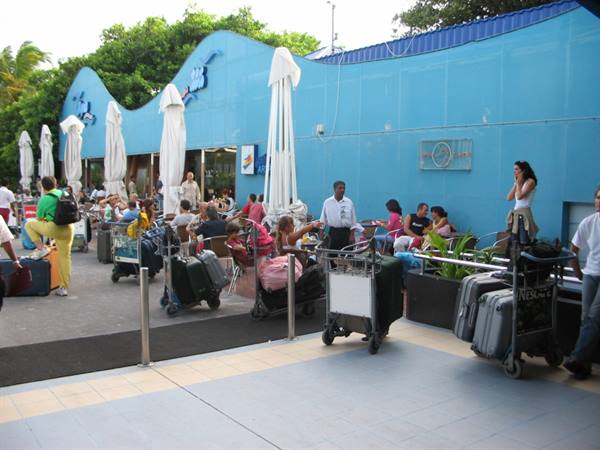 Travelers with luggage carts outside the blue terminal building at Malé airport