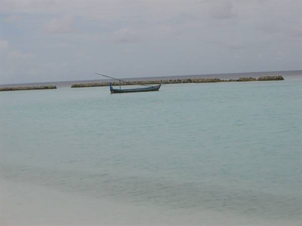 Blue boat anchored on turquoise water, stone breakwater in the background