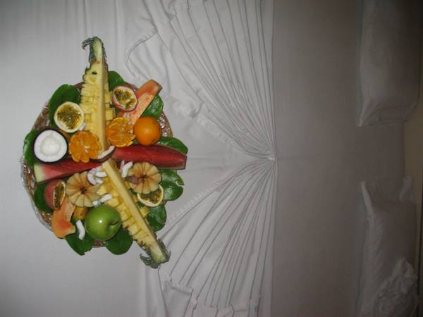 Basket of tropical fruit with pineapple, coconut and passion fruit on white bed