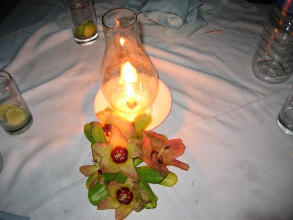 Glass lantern with lit flame and fresh flowers on white tablecloth