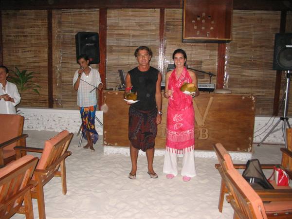 Couple holding coconuts inside a sand-floored bamboo beach bar