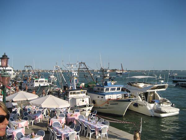 Restaurant tables under umbrellas beside moored fishing boats, Chioggia