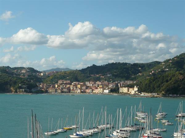 Sailboats moored in a marina, colorful houses and green hills behind