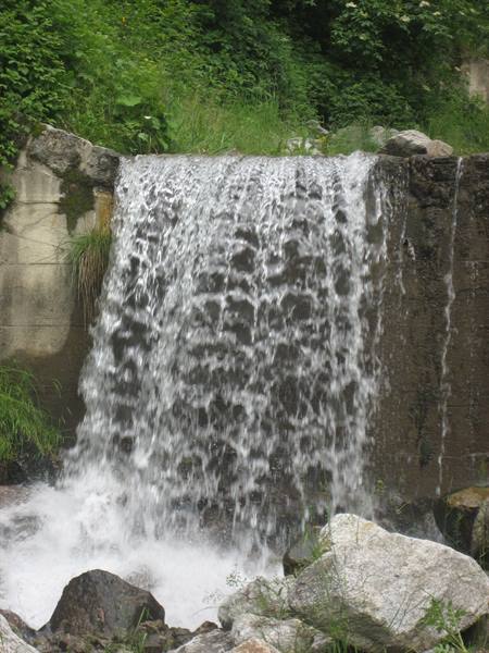 Foamy water spilling over a concrete weir among grass and boulders