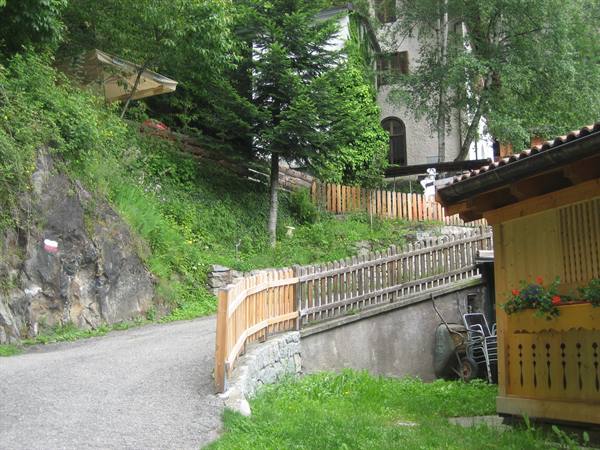 Gravel road with wooden fence, wooden chalet and houses among greenery