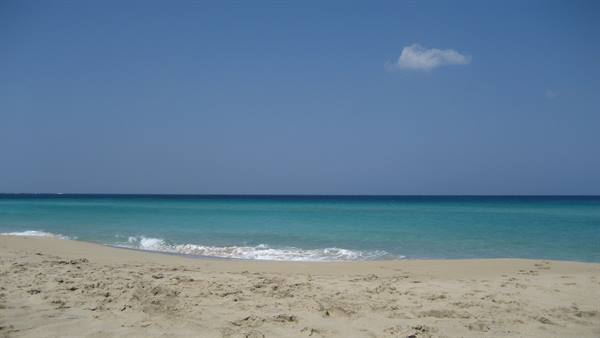 Small waves on pale sand, turquoise sea and blue sky with one cloud
