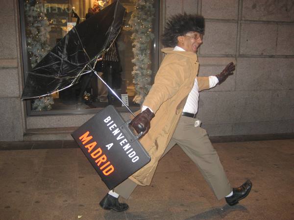 Man with inverted umbrella carries the Bienvenido a Madrid sign on the street