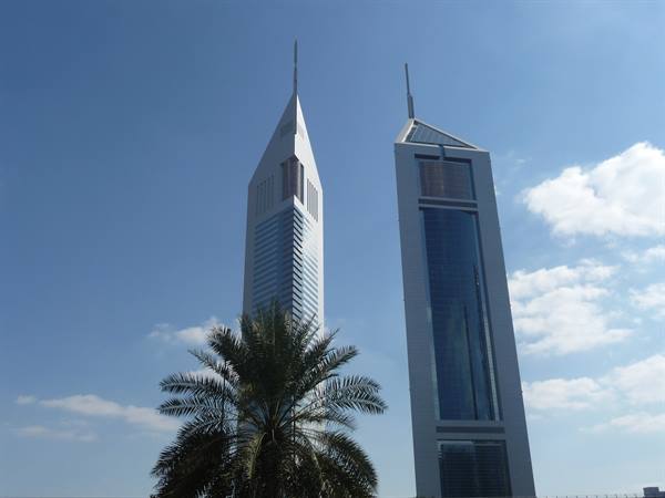 Emirates Towers glass skyscrapers rising behind a palm tree under blue sky
