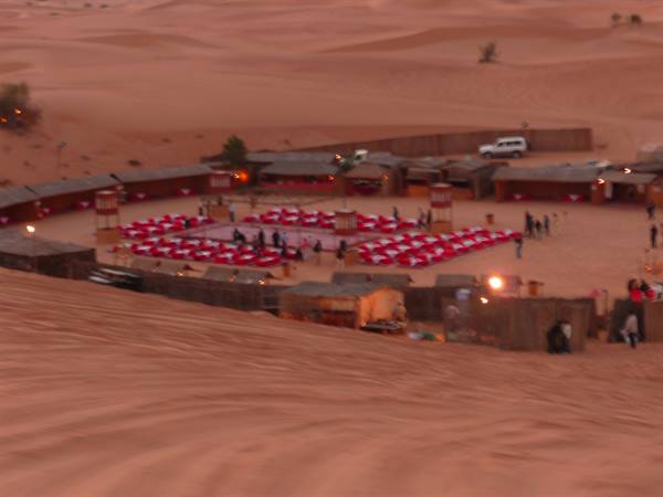 Bedouin camp among sand dunes, red chairs and lights at dusk