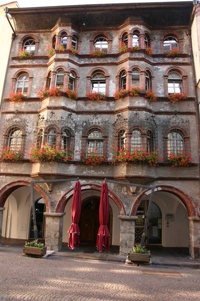 Old stone building with arched windows, red geraniums and arcades in Bolzano