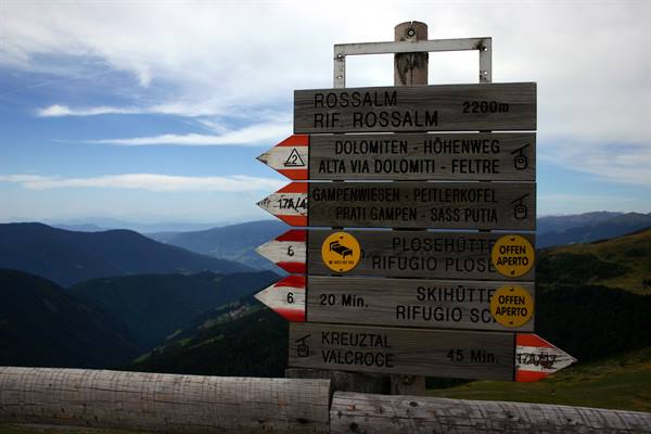Wooden signpost of Rossalm hut at 2200m, direction arrows against blue mountains