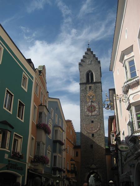 Stone clock tower between colorful houses in Sterzing