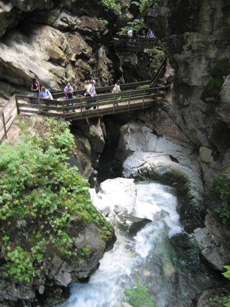 Tourists on wooden walkway above rushing stream between mossy rocks