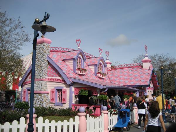 Pink and purple house with heart-shaped roofs, visitors and stroller near the white fence
