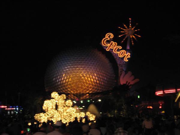 Spaceship Earth geodesic sphere lit at night with Epcot sign and crowd