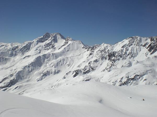 Snow-covered peaks under clear blue sky, fresh snow slopes in foreground