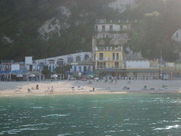Beach with umbrellas and colorful buildings at the cliff base, tourists in the sun