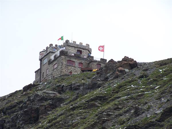 Stone building with battlements on rocky slope, Italian and Swiss flags
