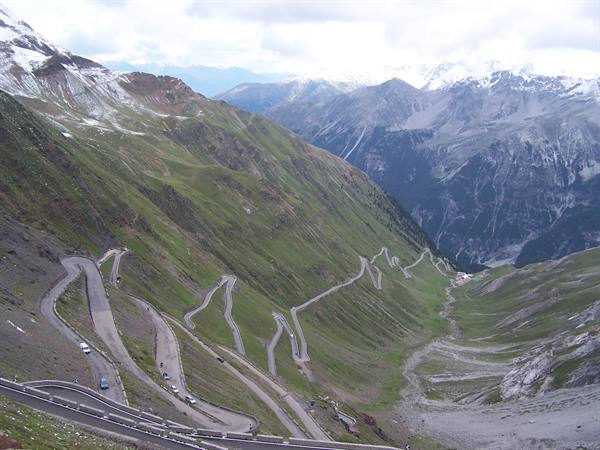Hairpin bends of Stelvio Pass, grey asphalt across green slopes and snowy peaks