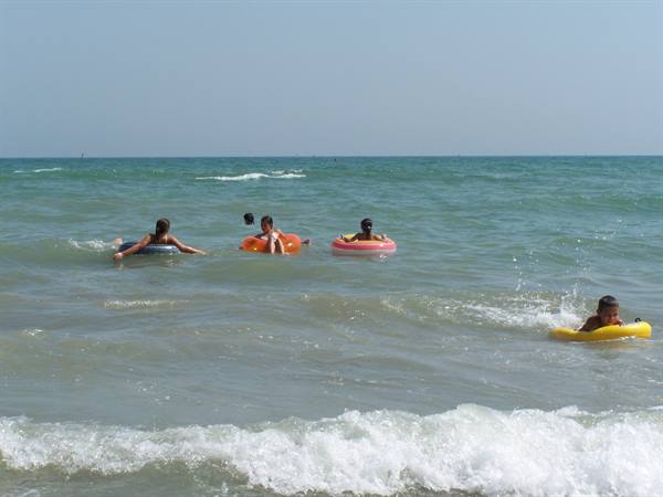 Children with colorful floats swim among the sea waves