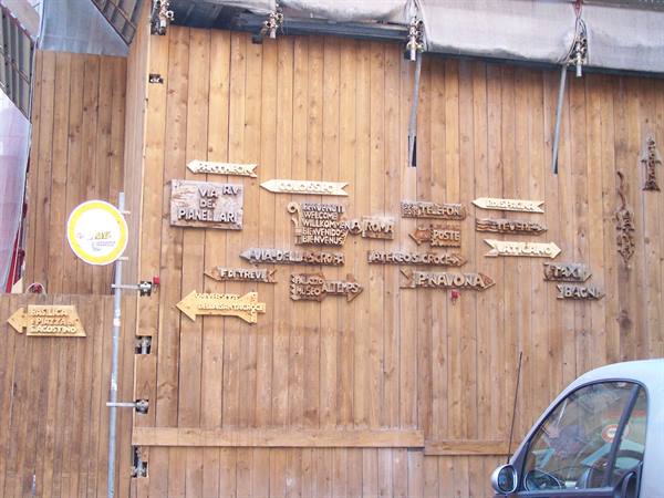 Wooden directional signs hanging on a brown plank wall beside a white car